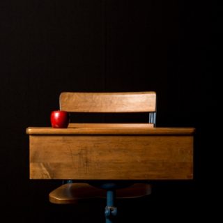 Eine hölzerne Schulbank vor schwarzem Hintergrund mit Apfel