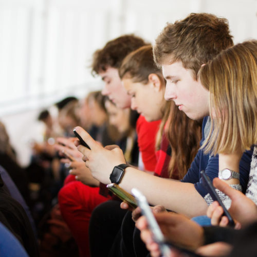 Junge Menschen sitzen gemeinsam da und schauen auf ihre Handys