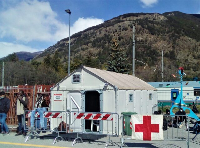 Ein Container des Roten Kreuzes vor hügeliger Landschaft.