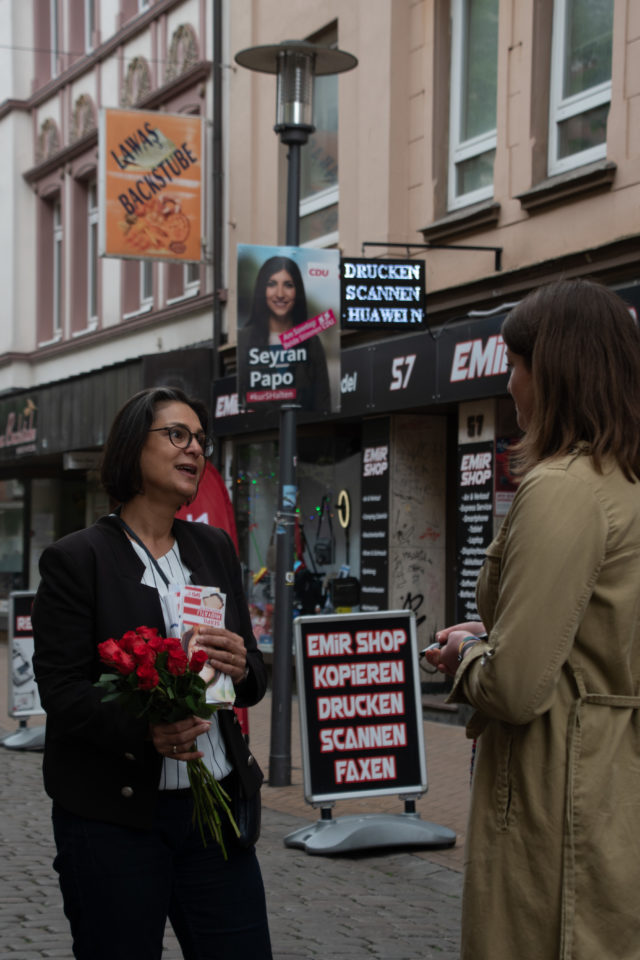 Eine Frau hält einen Bund rote Rosen in der Hand und spricht mit einer anderen Frau.