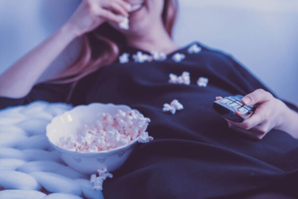 Eine liegende Frau isst Popcorn und hält eine Fernbedienung in der Hand.