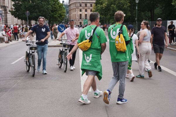 Volunteers in grünen T-Shirts laufen über die Straße der Fanmeile. 