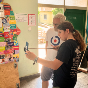 Redaktionsteilnehmer Klaas hält einen Selfiestick mit einem Handy in der Hand. Hinter ihm steht zur Unterstützung Christian von fjp>media. Beide schauen auf den Bildschirm des Handys.
